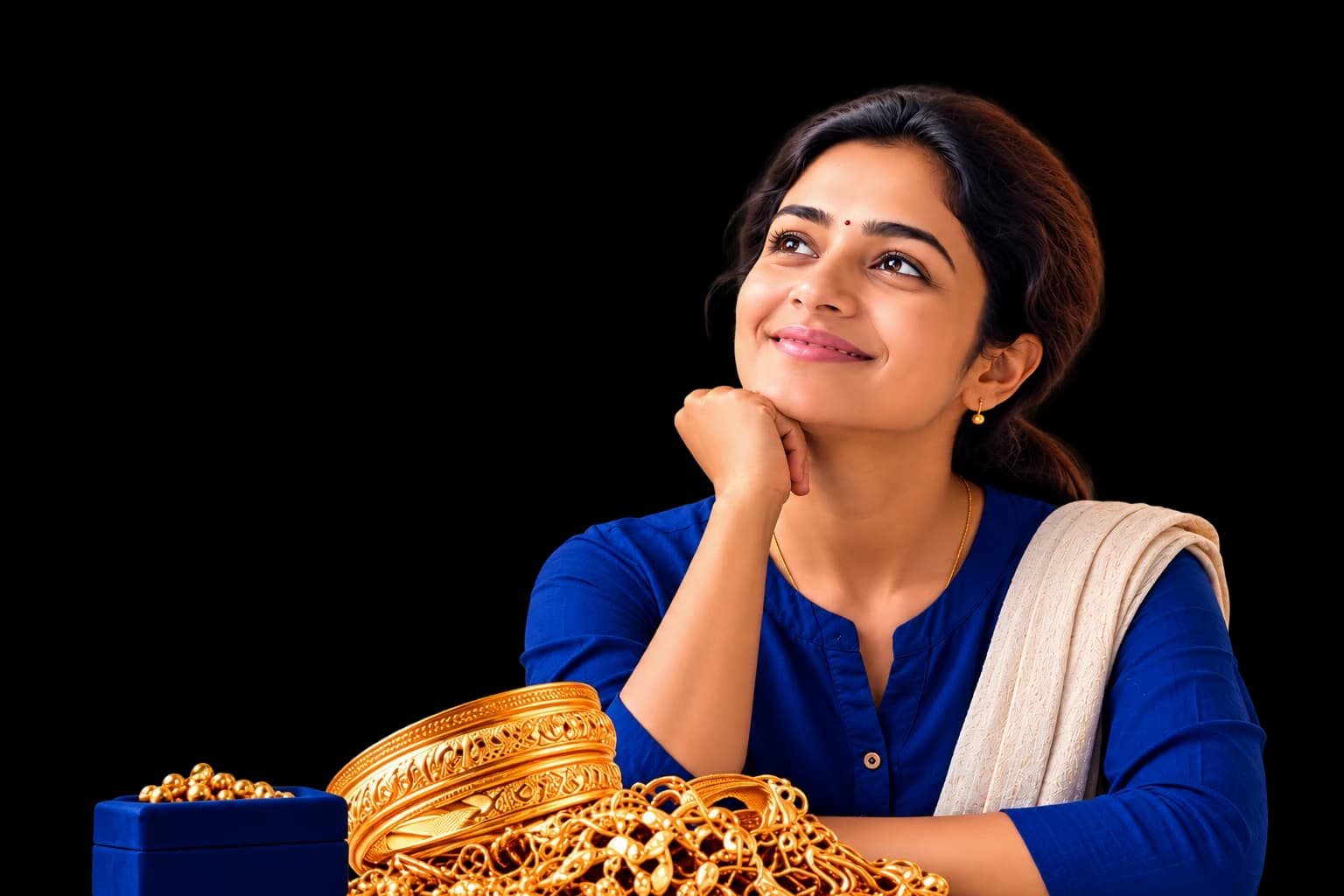 A smiling woman in a blue kurta rests her chin on her hand, gold bangles and chains on the table in front of her